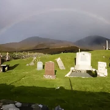 A rainbow over a cemetery with headstones in the foreground.